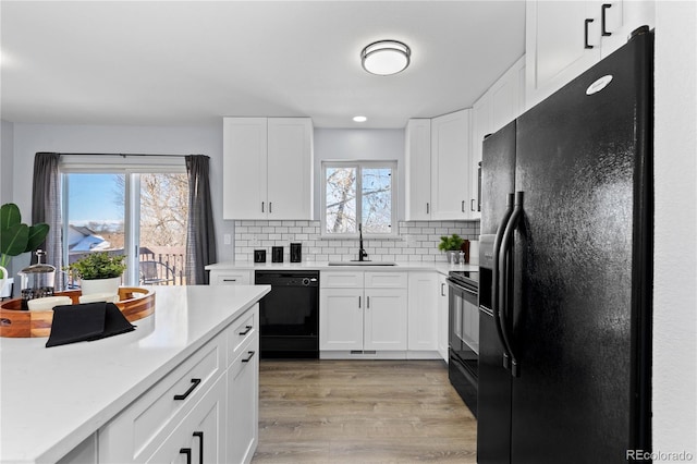 kitchen with light countertops, a sink, light wood finished floors, and black appliances