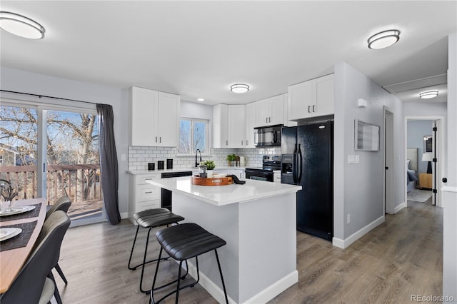 kitchen with tasteful backsplash, a breakfast bar area, white cabinetry, and black appliances