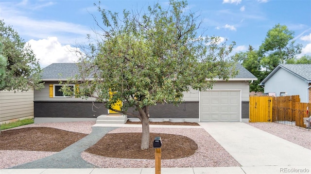 view of property hidden behind natural elements featuring brick siding, roof with shingles, an attached garage, fence, and driveway