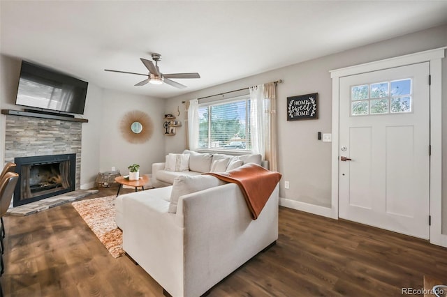 living area with a fireplace with raised hearth, ceiling fan, baseboards, and dark wood finished floors