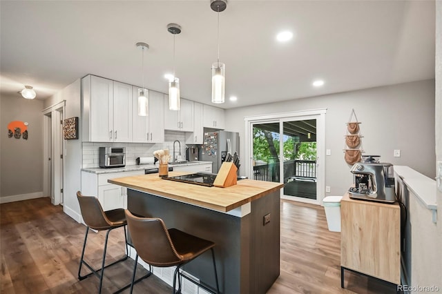 kitchen featuring wooden counters, white cabinetry, a sink, stainless steel fridge, and black electric cooktop