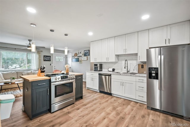 kitchen featuring light wood finished floors, decorative backsplash, white cabinets, appliances with stainless steel finishes, and a sink