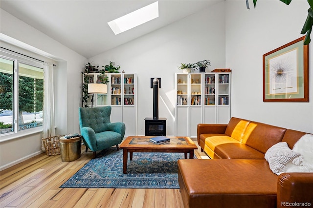 living room with a wood stove, a skylight, wood finished floors, vaulted ceiling, and baseboards