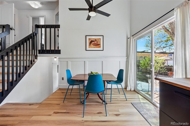 dining area featuring wood finished floors, ceiling fan, a high ceiling, a decorative wall, and wainscoting