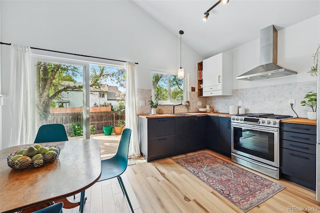 kitchen featuring wall chimney exhaust hood, gas stove, butcher block counters, a sink, and light wood-style floors