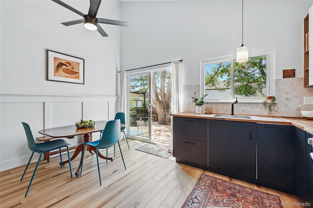 dining space featuring a towering ceiling, light wood-style flooring, a ceiling fan, a wainscoted wall, and a decorative wall