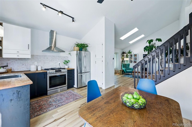 kitchen with appliances with stainless steel finishes, wall chimney range hood, light wood-style flooring, a skylight, and lofted ceiling