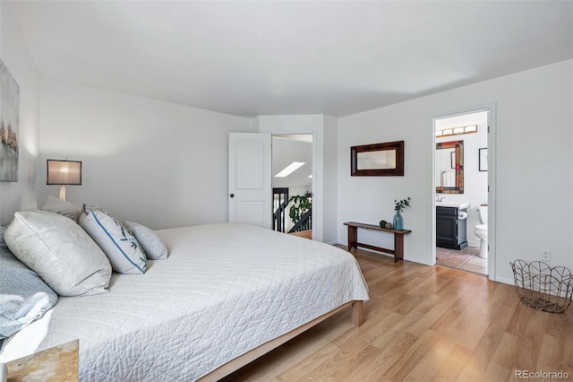 bedroom featuring light wood finished floors, baseboards, and ensuite bath