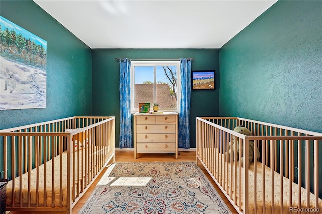 bedroom featuring wood finished floors, a textured wall, and a crib