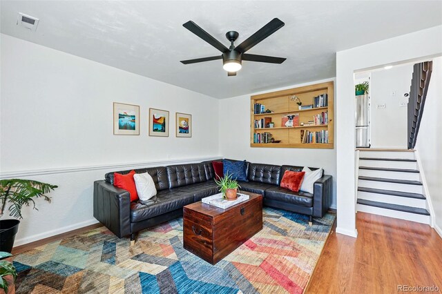 living room with wood finished floors, a ceiling fan, stairs, and baseboards