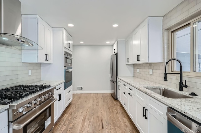 kitchen with light wood-type flooring, a sink, white cabinetry, stainless steel appliances, and wall chimney range hood