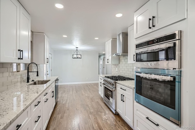 kitchen featuring light wood finished floors, a sink, stainless steel appliances, white cabinetry, and wall chimney exhaust hood