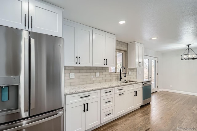 kitchen with tasteful backsplash, stainless steel appliances, wood finished floors, white cabinetry, and a sink