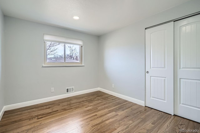 unfurnished bedroom with wood finished floors, visible vents, a closet, and baseboards