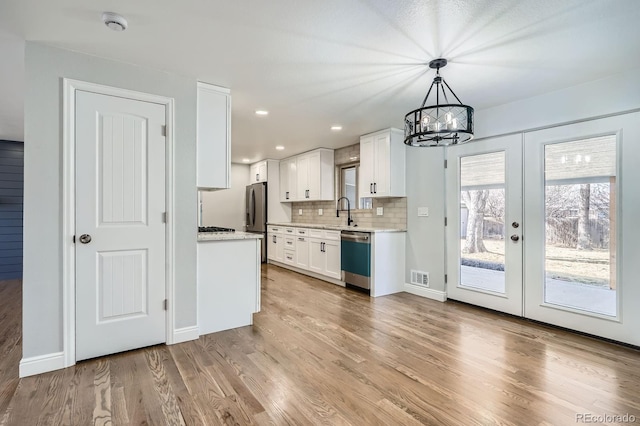 kitchen featuring tasteful backsplash, visible vents, light wood-type flooring, dishwashing machine, and freestanding refrigerator