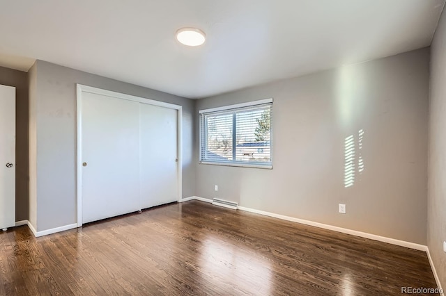 unfurnished bedroom with dark wood-style floors, a baseboard radiator, a closet, and baseboards