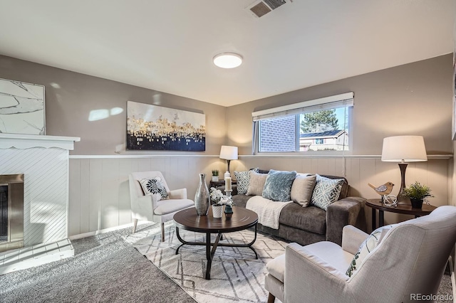 living area with a wainscoted wall, a tile fireplace, carpet flooring, and visible vents