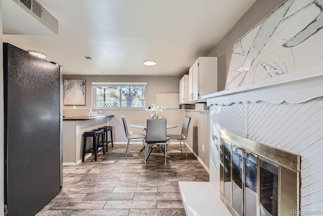 kitchen featuring freestanding refrigerator, white cabinets, visible vents, and wood finish floors