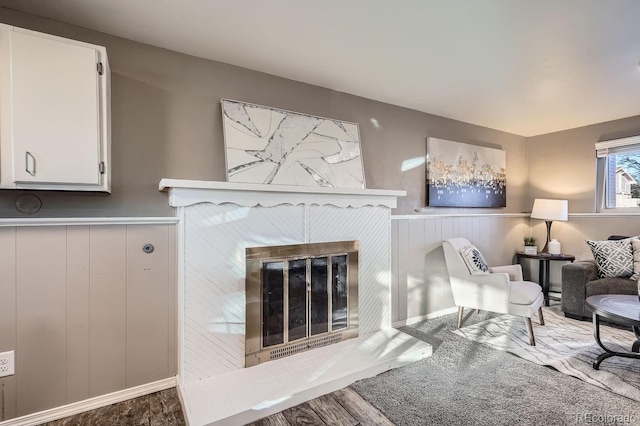 living room with a wainscoted wall, wood finished floors, and a glass covered fireplace