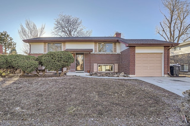 bi-level home with an attached garage, driveway, a chimney, and brick siding