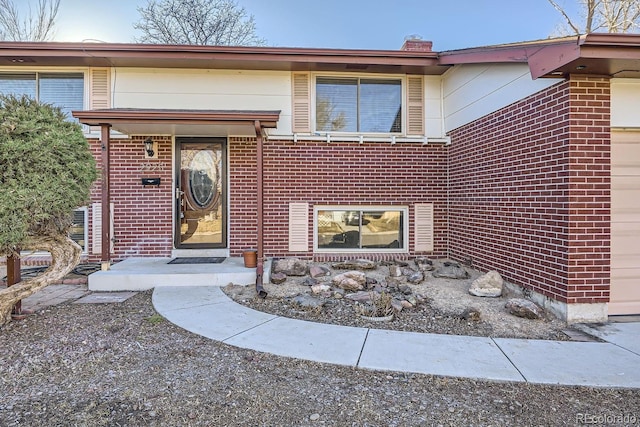 view of exterior entry with brick siding and a chimney