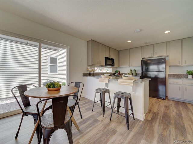 kitchen with stone counters, black appliances, a kitchen breakfast bar, kitchen peninsula, and light wood-type flooring