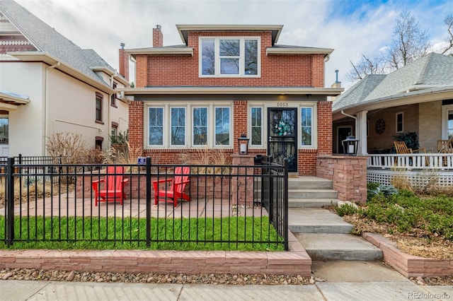 american foursquare style home featuring brick siding, a fenced front yard, and a chimney