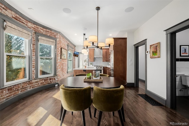 dining space with brick wall, baseboards, a chandelier, recessed lighting, and dark wood-style floors