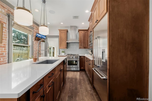 kitchen with visible vents, brick wall, a sink, built in appliances, and wall chimney range hood