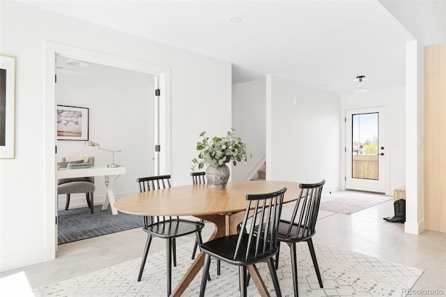 dining area featuring baseboards, concrete floors, and stairway