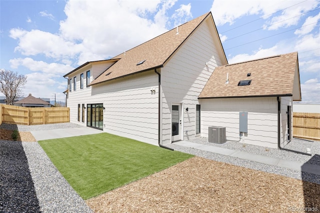back of house with central AC unit, a fenced backyard, a yard, a patio, and roof with shingles