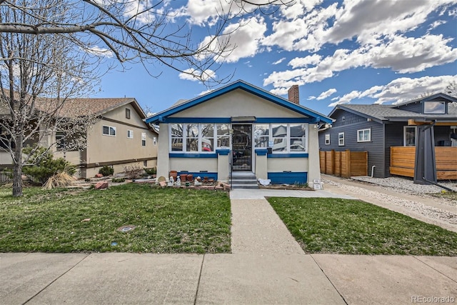 view of front facade with stucco siding, entry steps, fence, a front yard, and a chimney