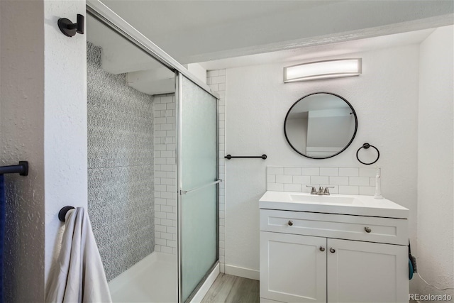 full bath featuring vanity, wood finished floors, baseboards, a shower stall, and backsplash