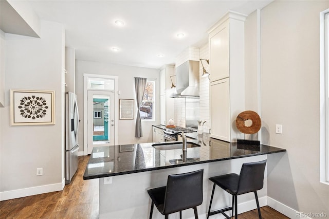 kitchen featuring white cabinetry, appliances with stainless steel finishes, kitchen peninsula, and wall chimney exhaust hood