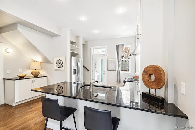 kitchen with kitchen peninsula, stainless steel fridge, sink, white cabinets, and dark stone counters