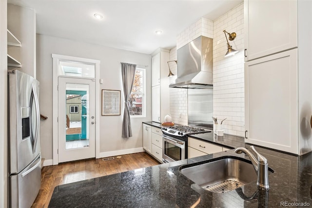 kitchen featuring white cabinetry, dark stone counters, sink, stainless steel appliances, and wall chimney exhaust hood