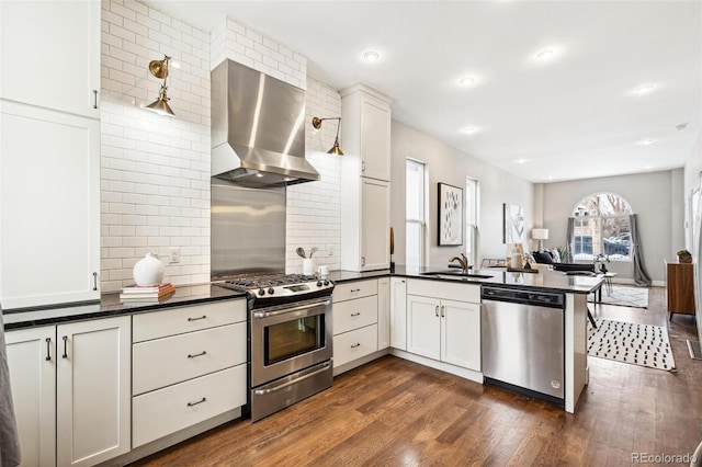 kitchen featuring wall chimney range hood, white cabinets, sink, kitchen peninsula, and stainless steel appliances