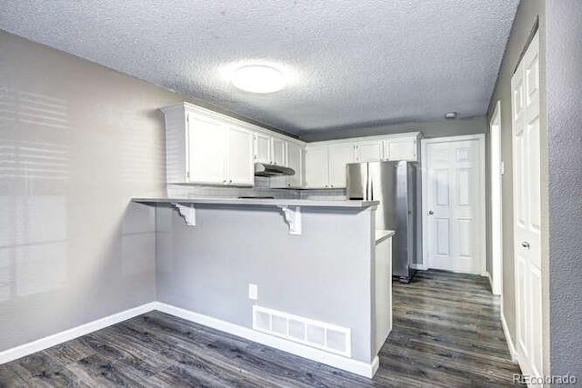 18131 E Arizona Ave Unit F, Aurora, CO 80017 - kitchen with freestanding refrigerator, a peninsula, dark wood-style flooring, under cabinet range hood, and a kitchen breakfast bar