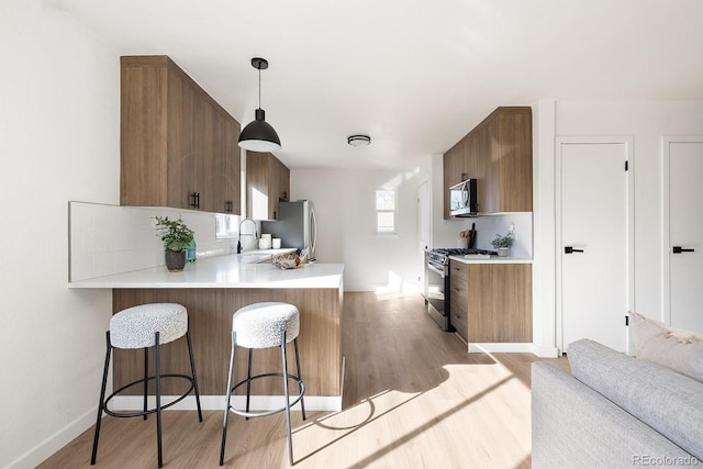 kitchen with a breakfast bar, a peninsula, stainless steel appliances, light countertops, and light wood-style floors