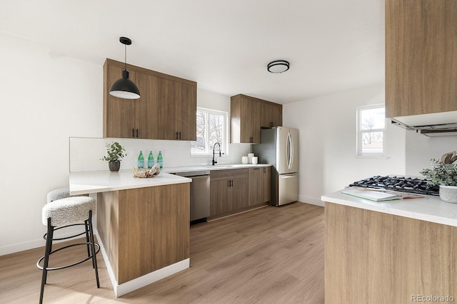 kitchen with stainless steel appliances, light wood-style flooring, decorative backsplash, a sink, and a peninsula