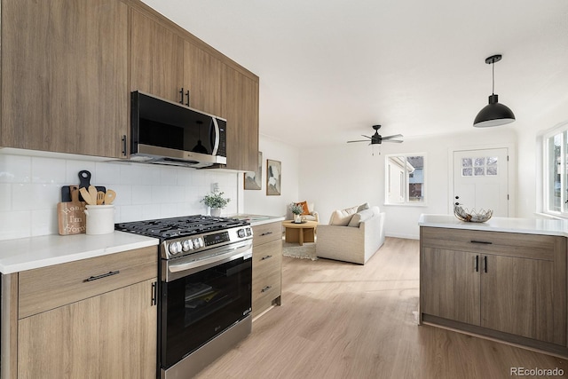 kitchen featuring open floor plan, light countertops, light wood-type flooring, stainless steel range with gas cooktop, and tasteful backsplash