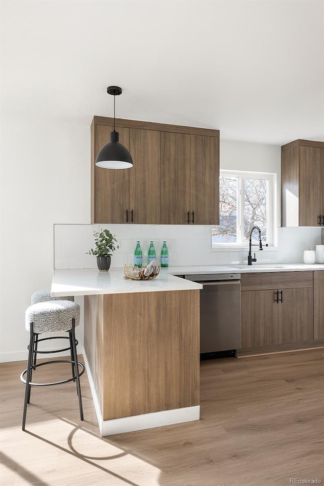 kitchen featuring light wood finished floors, light countertops, backsplash, stainless steel dishwasher, and a sink