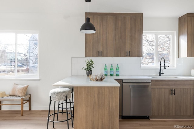 kitchen with light wood finished floors, dishwasher, a breakfast bar area, backsplash, and a sink