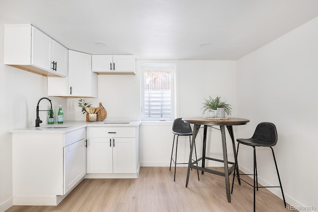 kitchen featuring a sink, white cabinetry, baseboards, light wood-style floors, and light countertops