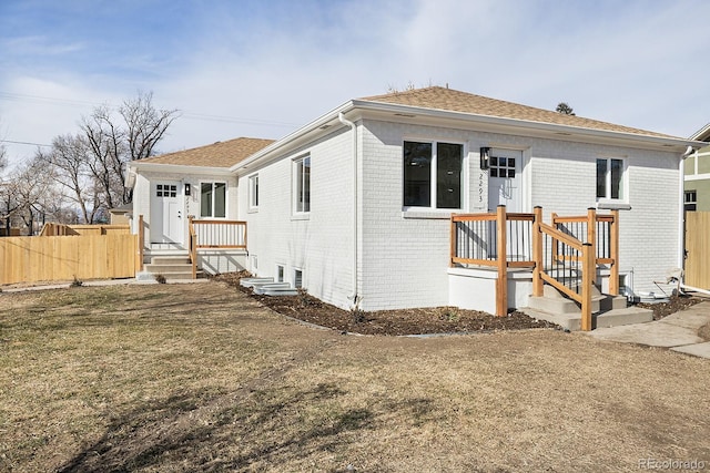 view of front facade featuring a shingled roof, brick siding, and fence