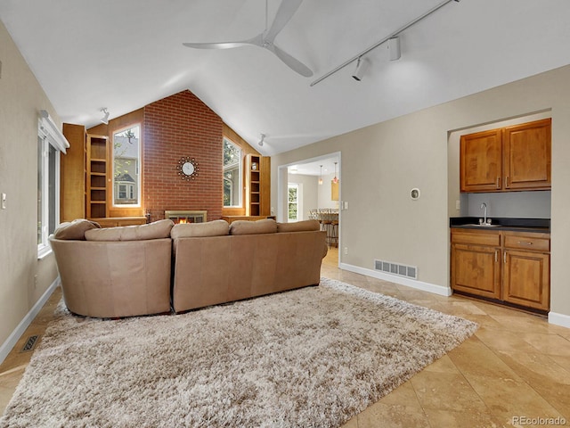 living room with a fireplace, a ceiling fan, vaulted ceiling, baseboards, and track lighting