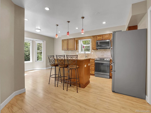 kitchen featuring stainless steel appliances, brown cabinetry, a kitchen island, a sink, and baseboards