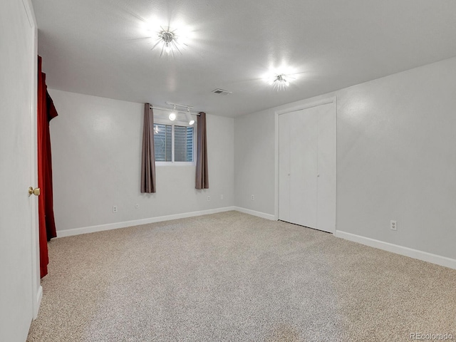 unfurnished bedroom featuring light carpet, rail lighting, and baseboards