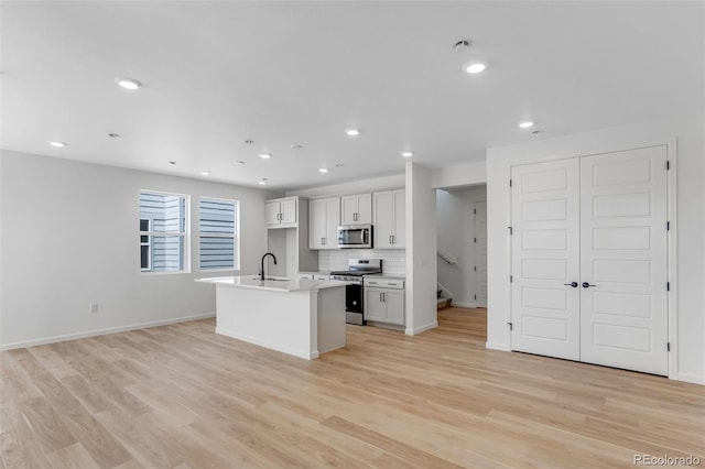 kitchen featuring stainless steel appliances, a sink, a kitchen island with sink, light countertops, and light wood-style floors