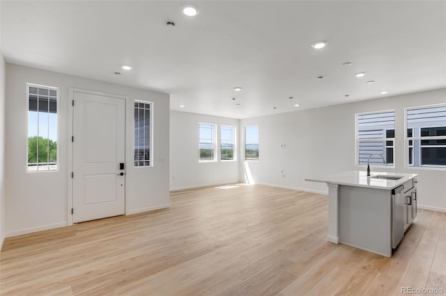 kitchen featuring a sink, light wood-type flooring, an island with sink, light countertops, and open floor plan